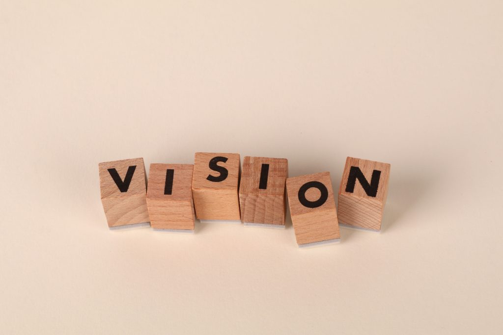 Wooden blocks with black letters spelling 'VISION' on a light beige background, symbolizing foresight and goals.